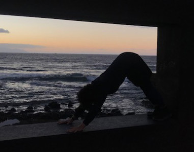 Mensch macht eine Yoga-Pose bei Sonnenuntergang am Strand.