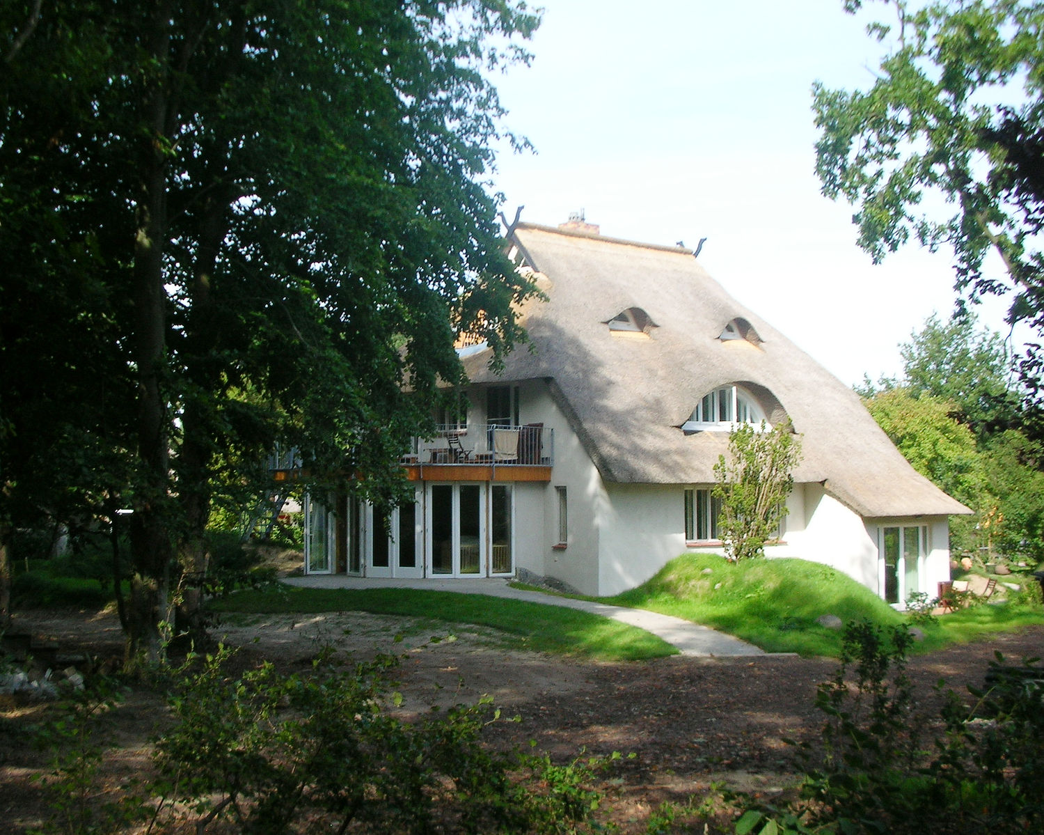 Von Natur und Laubbäumen beschütztes Haus der Alte Weberei Ahrenshoop, traditionell mit Reet bedeckt.